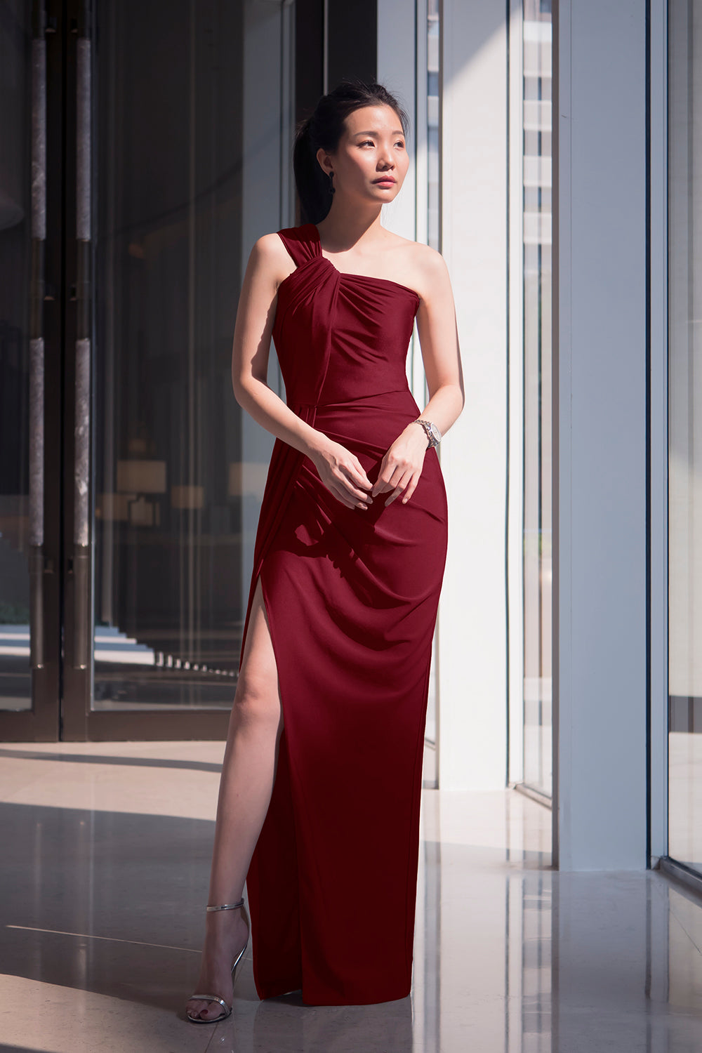 model in burgundy one shoulder with an asymmetric column skirt spandex evening dress