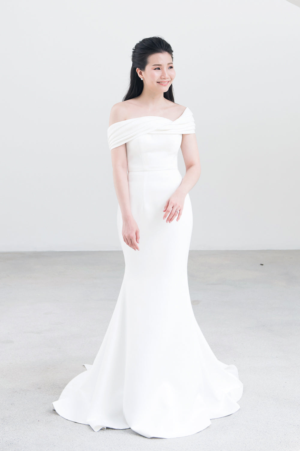 model wearing a white off the shoulder draped minimal wedding gown 