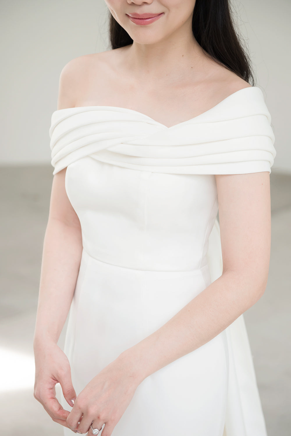 close up of a model wearing a white off the shoulder draped minimal wedding gown 